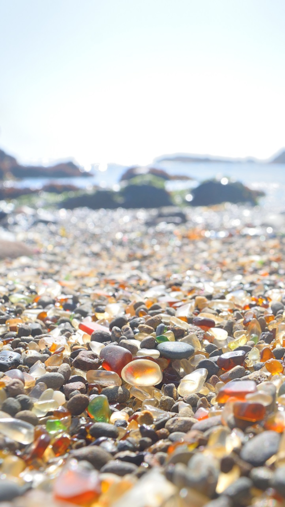 Rounded translucent pebbles of sea glass form a thin layer on the beach of a rocky cove in California.