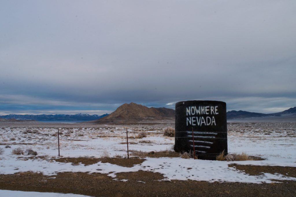 In a snow-draped desert, a sign behind a barbed wire fence says "Nowhere Nevada" and is underlined five times.